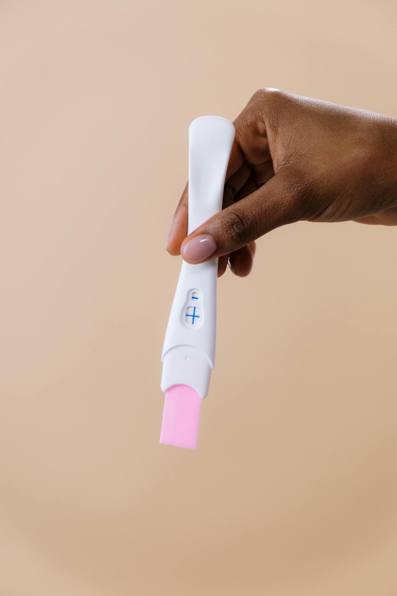 A close-up image of a hand holding a positive pregnancy test with a beige background.