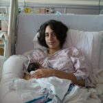 A new mother lovingly holds her newborn in a hospital setting post-delivery.